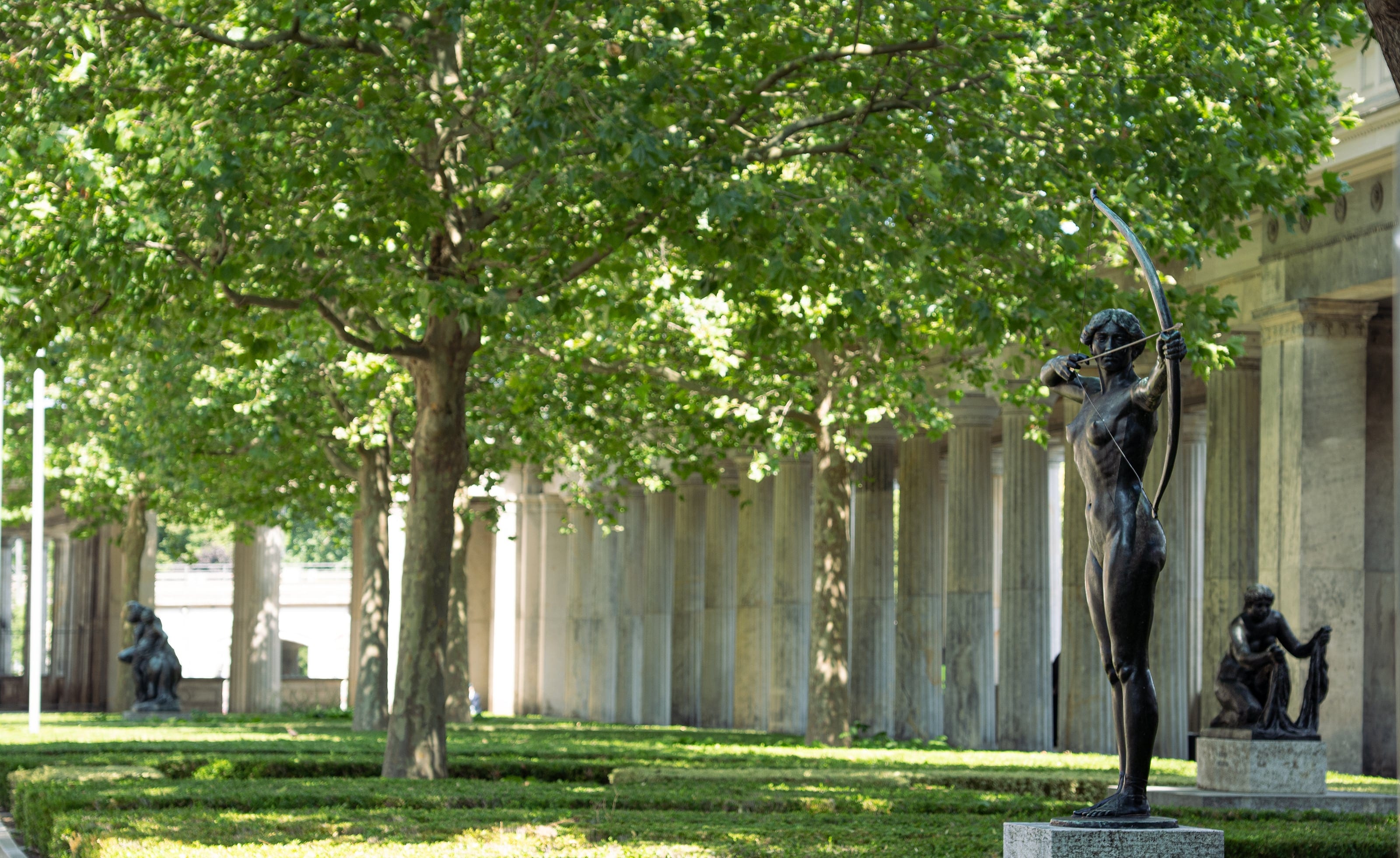 A statue among plane trees beside a colonnade