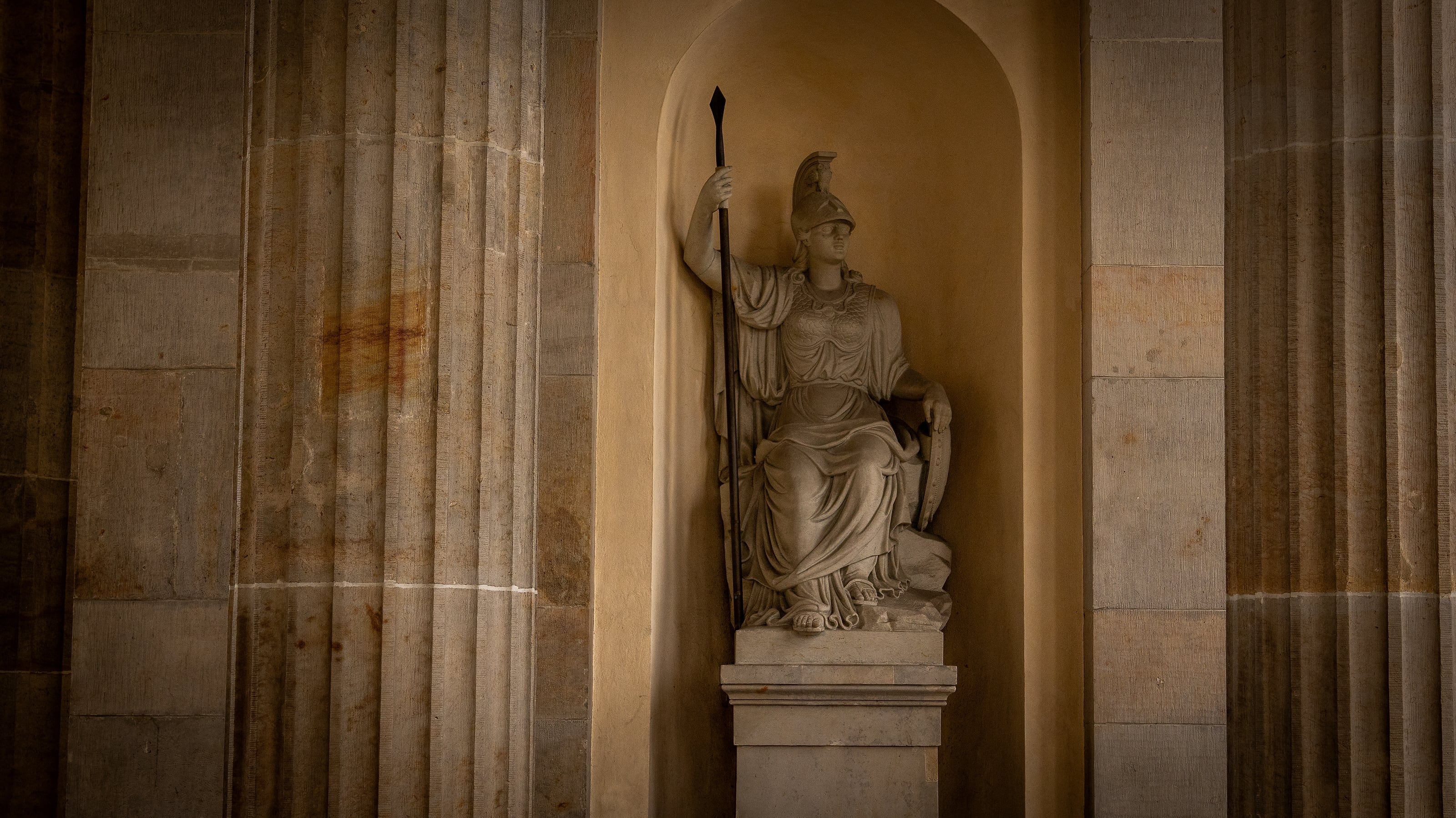 A seated statue of a helmeted goddess in a columned niche